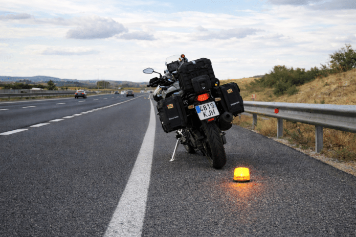 Moto detenida en el arcén de una autopista con baliza luminosa activada, ejemplo práctico de cómo señalizar un accidente en moto de forma segura.